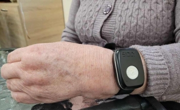 Teleopieka dla osób starszych dłoń starszej osoby. Na ręce założona opaska SOS